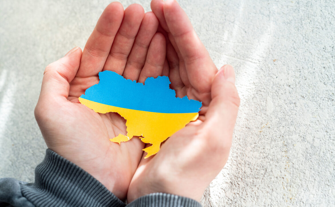 Hands holding the national flag of Ukraine in the shape of the b
